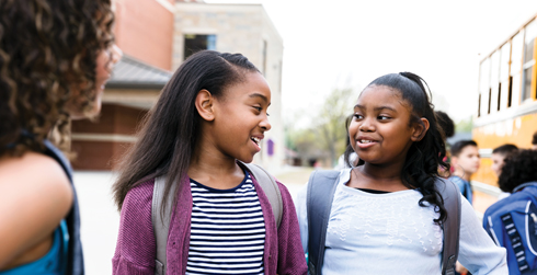 Group of young girls chatting in front of school bus, school setting