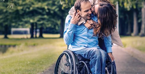 Man in wheelchair with woman hugging him from the side.