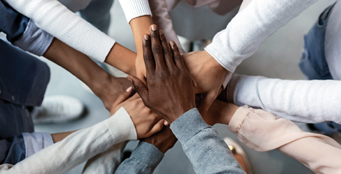 Diverse hands meeting in the middle of a circle, one on top of the other.