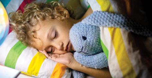 Child sleeping in bed with stuffed bunny