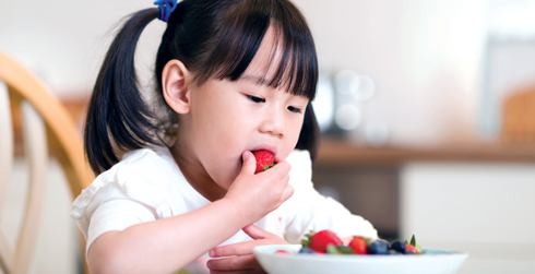 Child sitting at table eating a bowl of strawberries