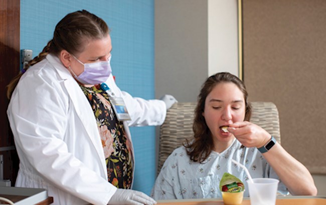 Occupational therapist evaluating patient eating applesauce during a tableside dysphagia assessment.
