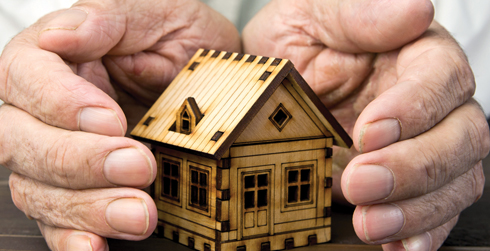 A pair of hands surrounding a tiny house made of wood.