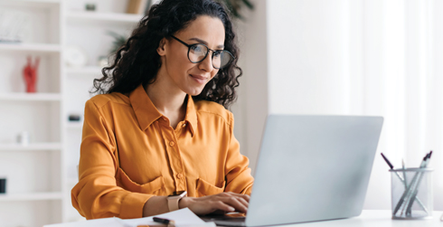 Woman with glasses sitting in front of laptop and typing